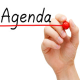 person writing word "agenda" on a whiteboard